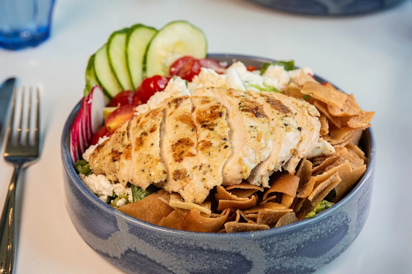 Grilled chicken over a colorful salad with cucumbers and crisp pita chips